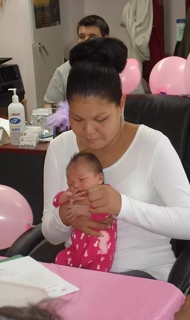 A woman holding a baby with pink balloons all around her